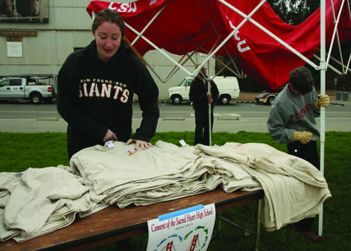 Senior Kristy Harty-Connell folds Walk for Uganda T-shirts as CSH teachers put up a tent in the background. Around 30 students gathered at Crissy Field to participate in the third annual fundraiser despite inclement weather. ZOE NEWCOMB | the broadview