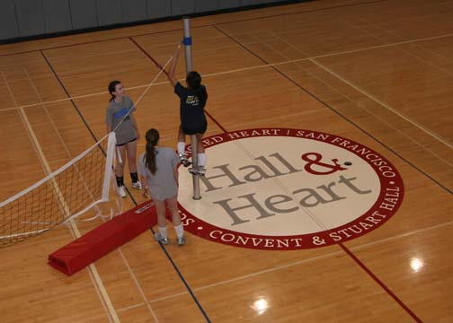 JEWEL DEVORAWOOD | the broadview. JV volleyball team sets up the net next to the Heart & Hall logo in the Herbert Gym. Another additon to the gym is the red padding on the bleachers. 
