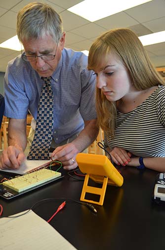Rooney works with physics student Caitlin Martin on a circuit lab, checking the current that flows through each resistor with a meter. Along with teaching Rooney is also plays guitar for Joyful Noise!