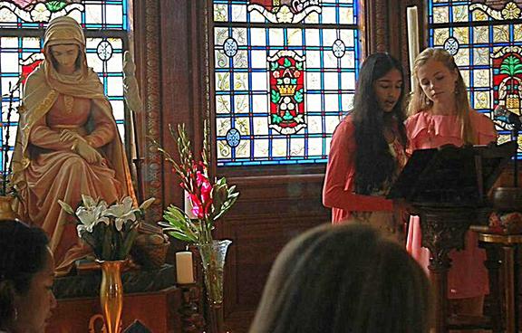 Freshmen Asha Khanna and Lily Niehaus open yesterday's prayer service for the Feast of Mater Admirabilis with the Call to Prayer. The statue is a likeness of the fresco in Rome, painted in 1844 by Pauline Perdrau.