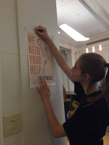Senior Catherine Heinen tapes a promotional poster for the toiletry drive. Boxes are located in the library, gallery conference room and den.