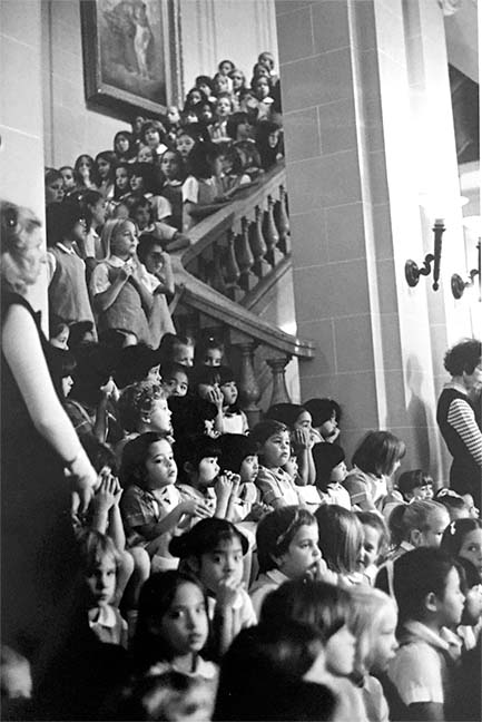 Elementary school students sit on the Marble Stairs as part of the 1977 Noëls celebration. Students wore white dresses for the occasion, unlike the dress uniform students wear today.