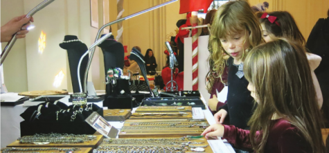 Kindergartners Rebecca Alba (left) and Elaine Roberts (right) admire the necklaces at one of the booths in the Main Hall. The Merry Marketplace was set up on Dec. 5 for members of the Sacred Heart community to take part in a Christmas boutique. Boots, food truck and games were part of the event. The items for sale ranged from jewelry to books to toys for children.