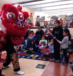 Two girls feed cabbage to a lion dancer from the Jing Mo Athletic Association during a performance at the Glen Park Public Library. The martial arts group performs lion dances at the library annually.