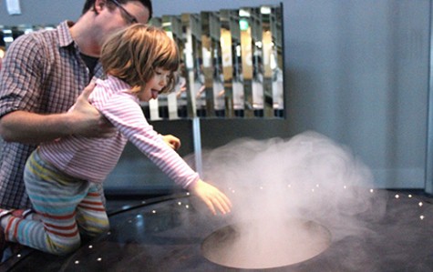 A father-daughter duo at the Exploratorium inspects a steam machine that functions as a study on atmosphere in the front gallery. 