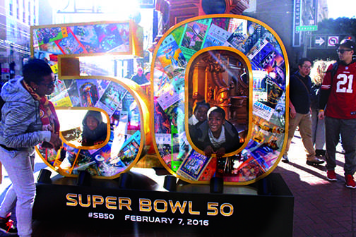 Football fans pose in front of Super Bowl installation at Pacific Avenue and Kearny Street. City officials working for the Super Bowl City stand at these installations and take photos for fans. 