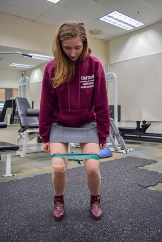 Senior Cat Heinen squats with a stretch band in order to help re-align her knees from patellofemoral syndrome, knee pain caused by outer leg muscles pulling the kneecaps the wrong way. Heinen performs a set of exercises and stretches every day including squats and leg extensions.