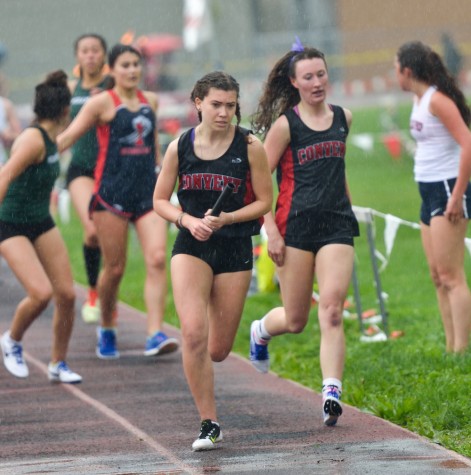 Five girls beat their personal bests. Junior Ana Cahuas receives the baton from senior Mae Singer while racing in the rain.