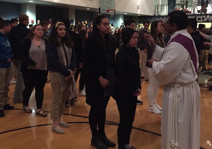 Senior Sarah Hong receives ashes from celebrant Eddy Gutierrez in  The Dungeon. Convent students were transported to Stuart Hall on school buses.