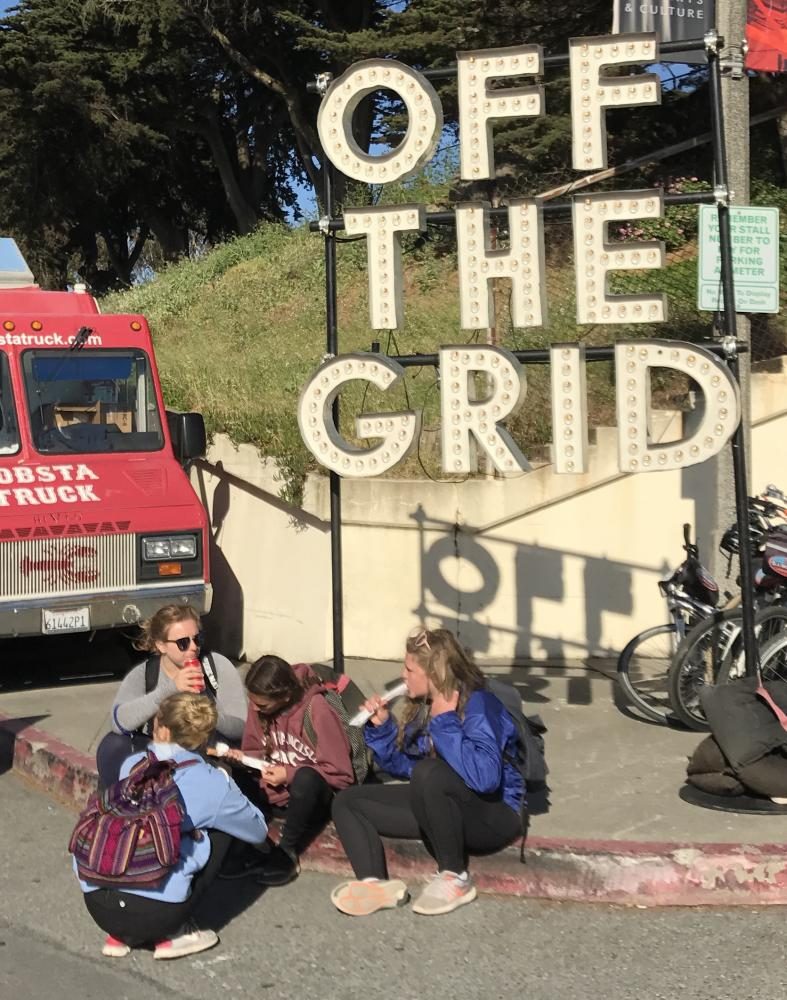 A group of girls eat churros from a nearby food truck while sitting in front of the Off the Grid sign. Off the Grid occurs at Fort Mason every Friday from 5-10 pm.