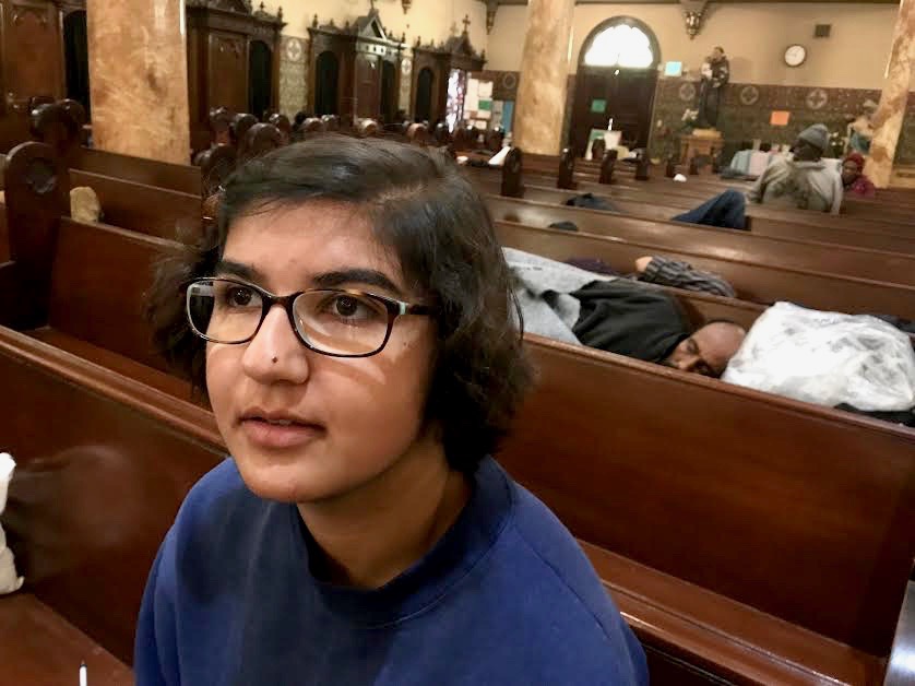 Sophomore Arianna Nassiri sits in a pew in front of men taking part in the Gubbio Project at St. Boniface Church. The Gubbio Project worked with St. Boniface to provide a safe and quiet space for homeless people to rest during the day.