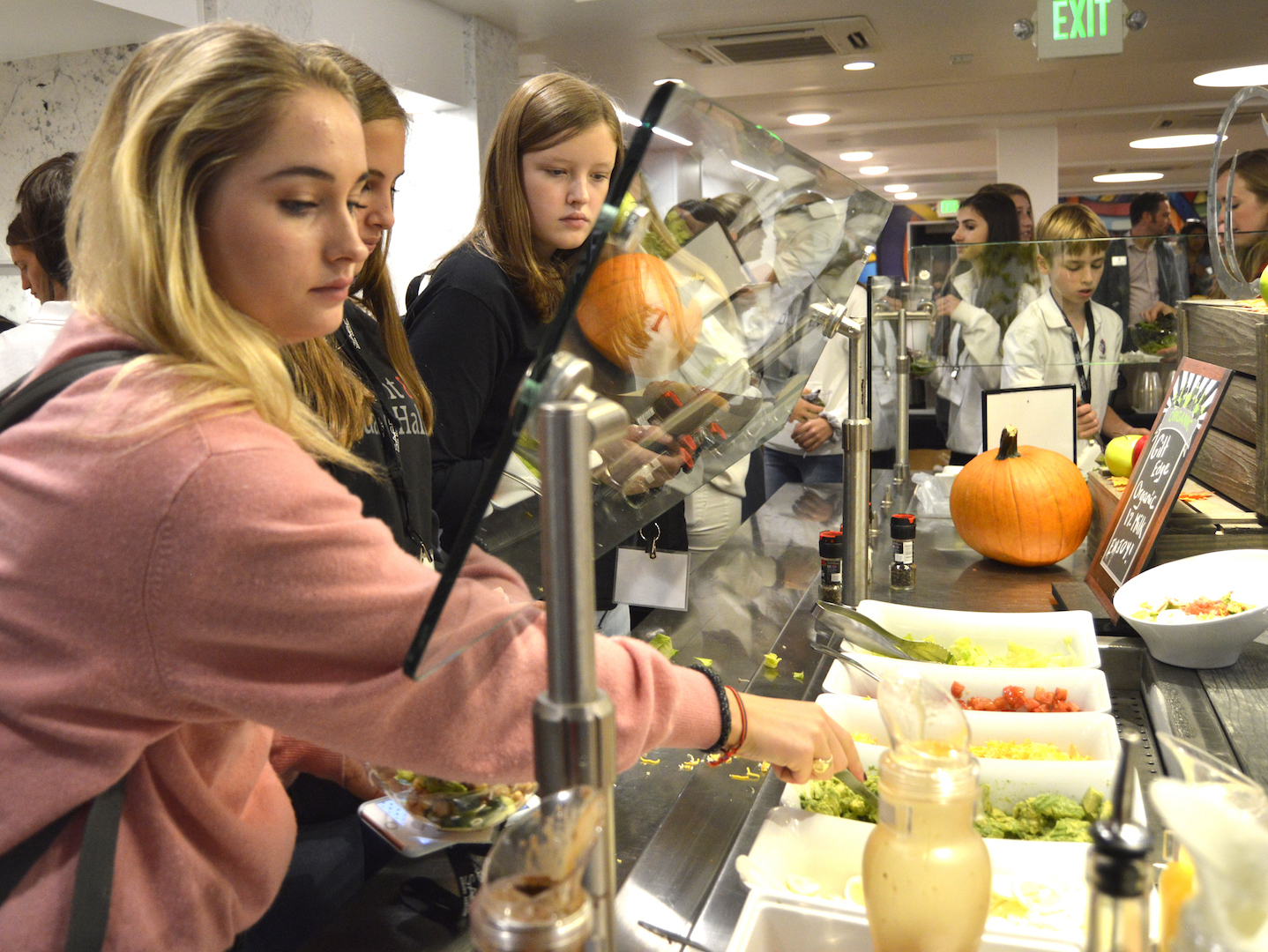 Senior Caroline Schulberg adds avocado chunks and other toppings to her salad from the cafeteria's build-your-own salad bar. Students wear lanyards with their name and photo on them to show that they have paid for the meal plan.