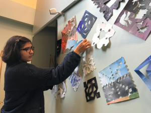 Junior Arianna Nassiri tapes snowflakes on the wall outside of the Syufy Theater for the art show. The exhibit will open on Dec. 12.