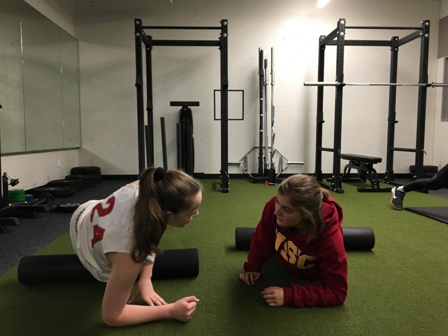 Sophomore Cecilia McQuaid and junior Sofia Telfer stretch in the weight room in the Herbert Center. The new mural will be painted on the back wall of this room. 