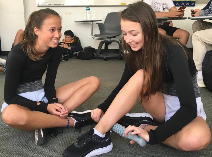 Freshman Amelia Abernethy and Madeline Thiara stretch and use the muscle roller stick before practice on Tuesday. Yesterday runners had twin day to celebrate track and field’s spirit week.