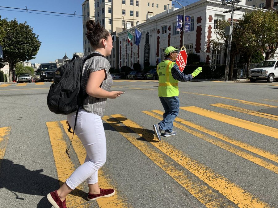Senior Dena Silver crosses the intersection of Broadway and Webster streets with the help of a crossing guard. Traffic commissioners work during drop-off and pick-up to ensure safety.