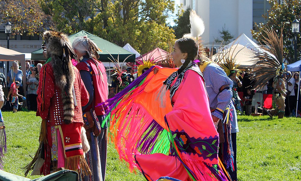 Indigenous People’s Day being celebrated in Berkeley, USA with a sacred dance preformed by an Indigenous tribe member in a colorful regalia. Tribes native to California include Karok, Maidu, Mojave, Yokuts, and Modoc, among many others.