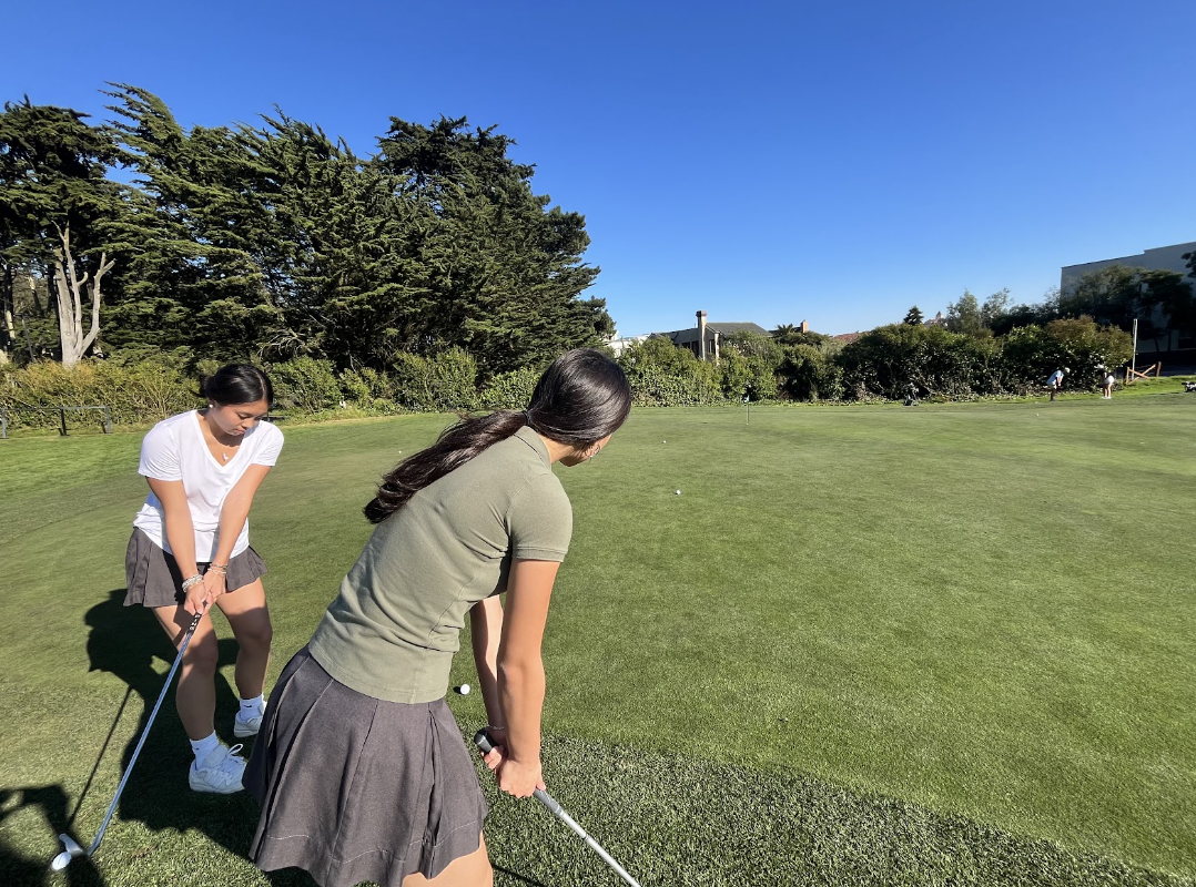 Sophomores Vivienne Tang and Sophia Lum hit balls during JV golf practice in their modified dress code. Today the temperature reached 92 degrees.