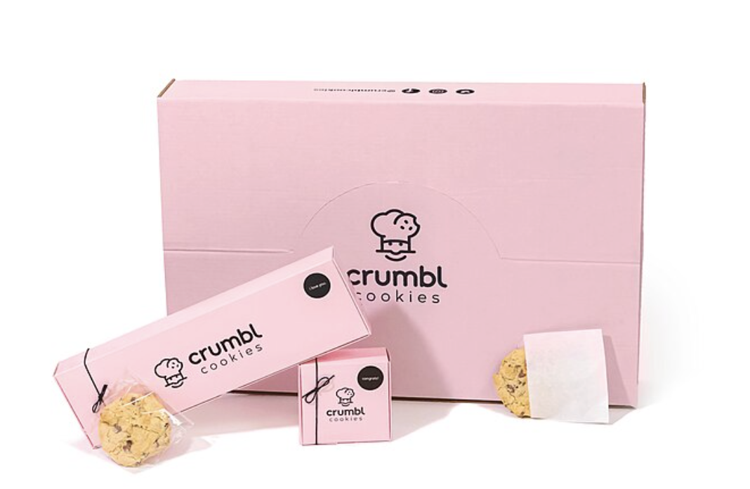 The classic pink Crumbl Cookies boxes are displayed. They show the single cookie box, the 4 pack and the party pack.