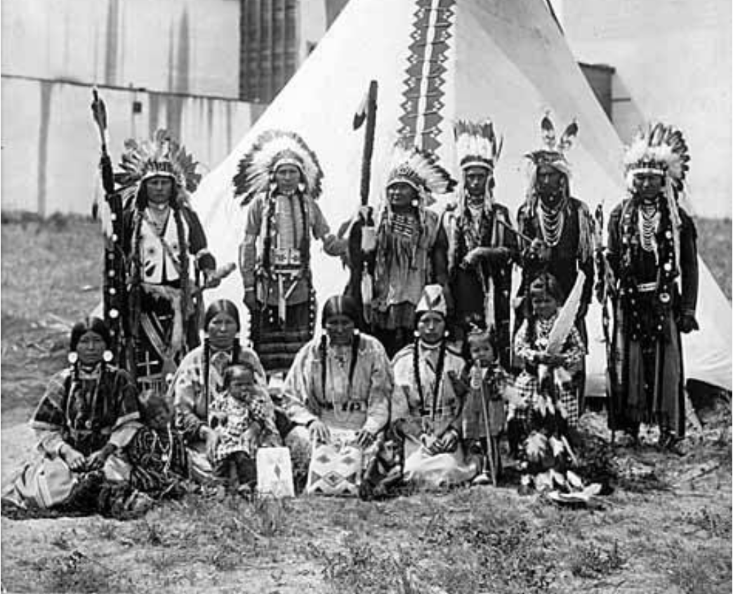 Native Americans of all ages wear tribally specific ceremonial dress. A historical group of Umatilla and/or Nez Perce members are seen here, representing the traditional context of regalia and indigenous garments.